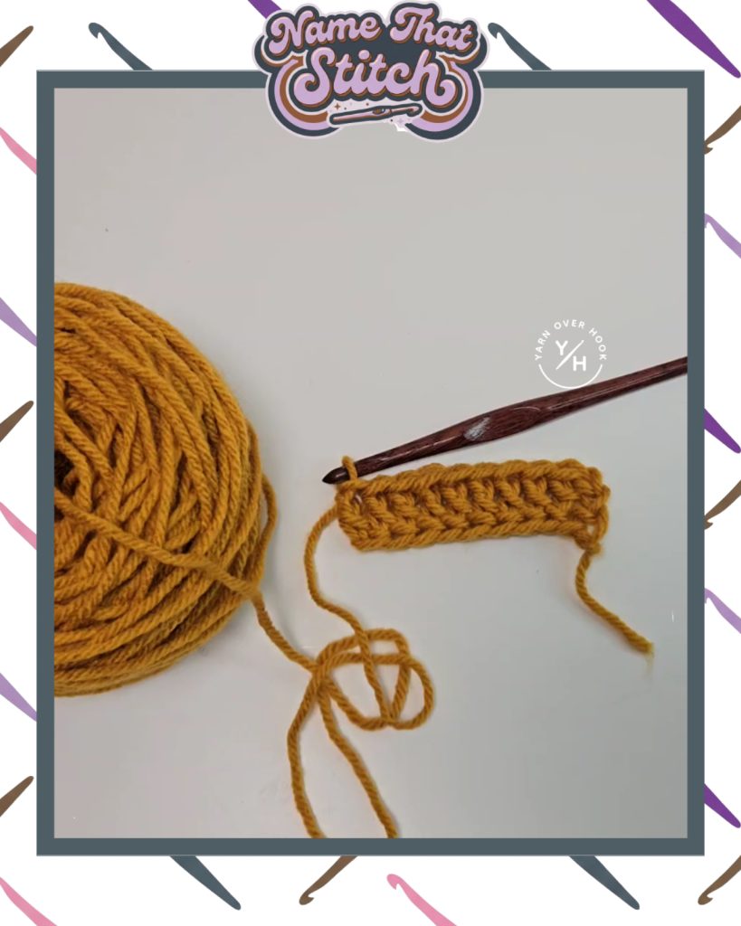 Close-up of a crochet work-in-progress showing a short row of textured stitches in mustard yellow yarn, with a wooden crochet hook and yarn ball, featured as part of the Name That Stitch daily crochet puzzle. View more at NameThatStitch.com
