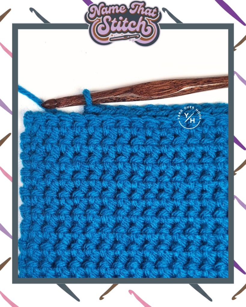Close-up of a crochet work-in-progress showing a short row of textured stitches in blue yarn, with a wooden crochet hook and yarn ball, featured as part of the Name That Stitch daily crochet puzzle. View more at NameThatStitch.com