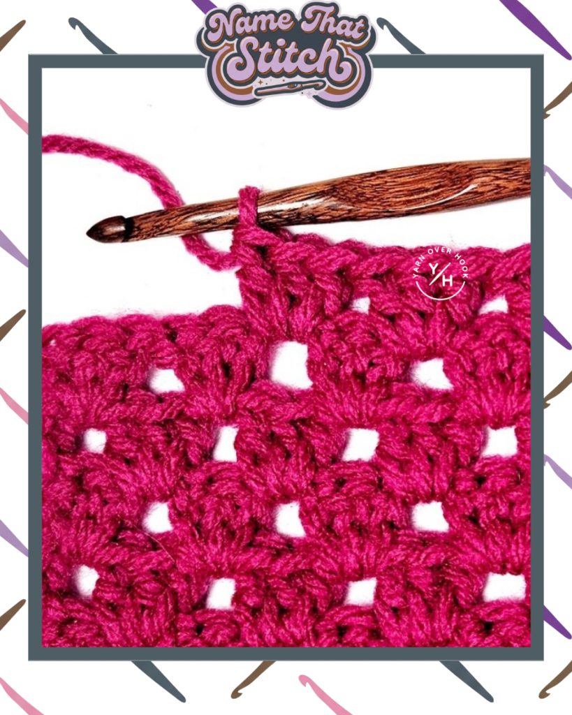 Close-up of a crocheted fabric displaying a repeating stitch pattern worked in a cranberry yarn, with a wooden crochet hook and featured as part of the Name That Stitch daily crochet puzzle. View more at NameThatStitch.com