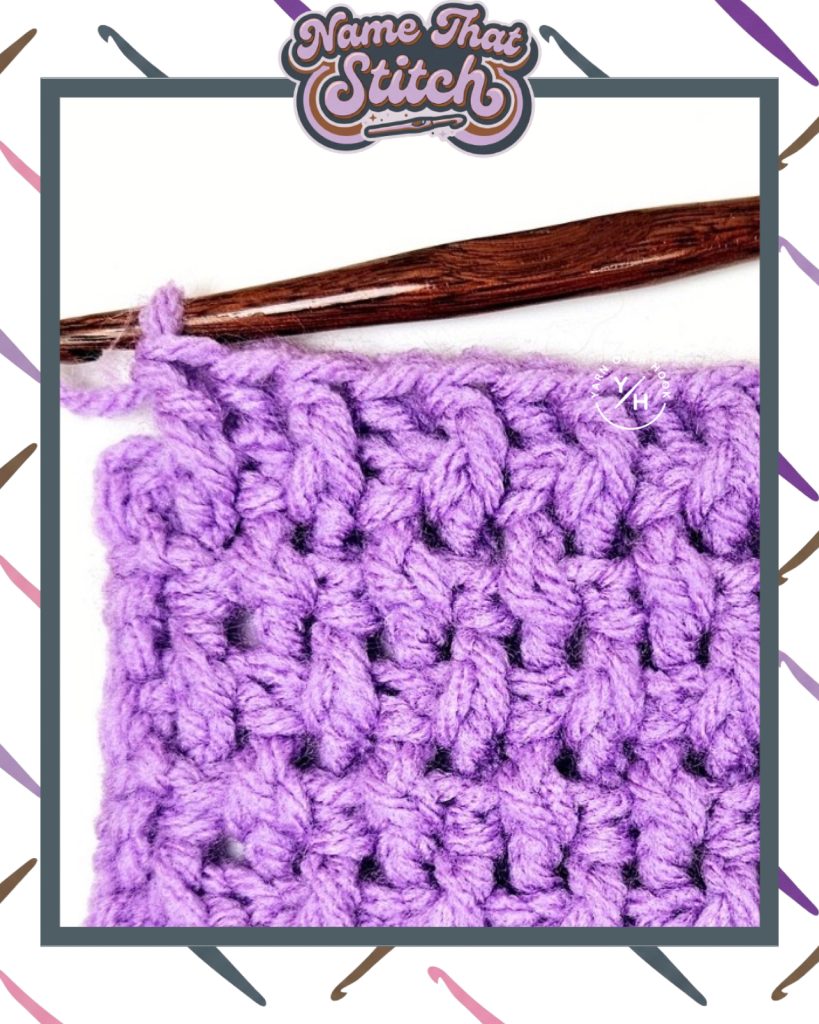 Close-up of a crocheted fabric displaying a repeating stitch pattern worked in light purple yarn, with a wooden crochet hook and featured as part of the Name That Stitch daily crochet puzzle. View more at NameThatStitch.com