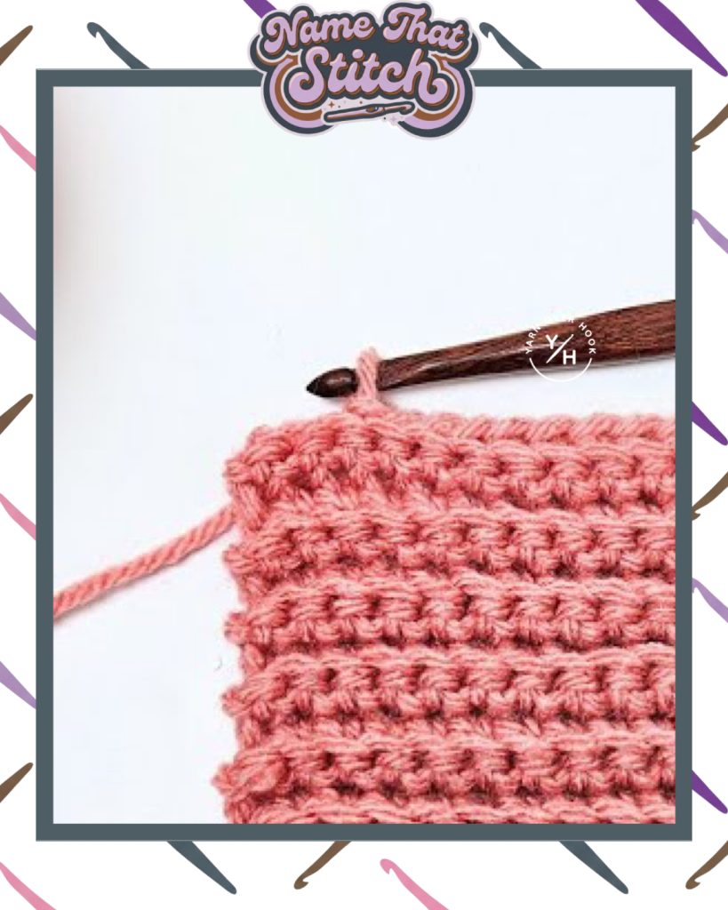 Close-up of a crocheted fabric displaying a repeating stitch pattern worked in light pink yarn, with a wooden crochet hook and featured as part of the Name That Stitch daily crochet puzzle. View more at NameThatStitch.com