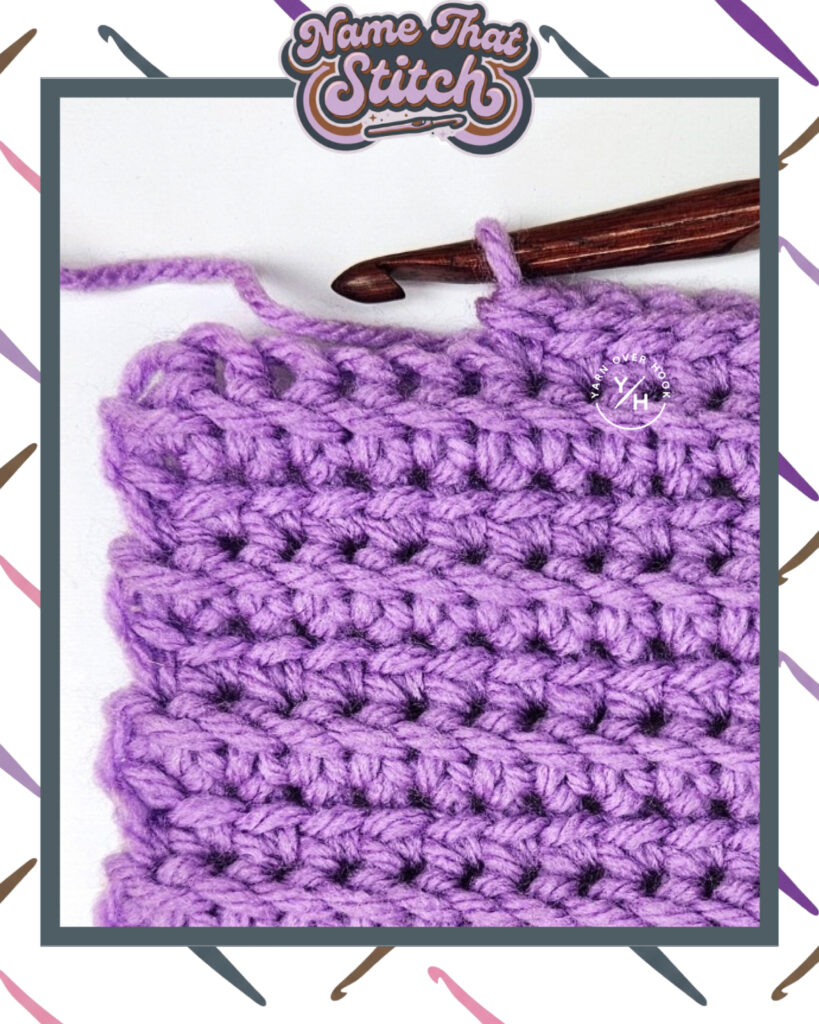 Close-up of a crocheted fabric displaying a repeating stitch pattern worked in purple yarn, with a wooden crochet hook and featured as part of the Name That Stitch daily crochet puzzle. View more at NameThatStitch.com