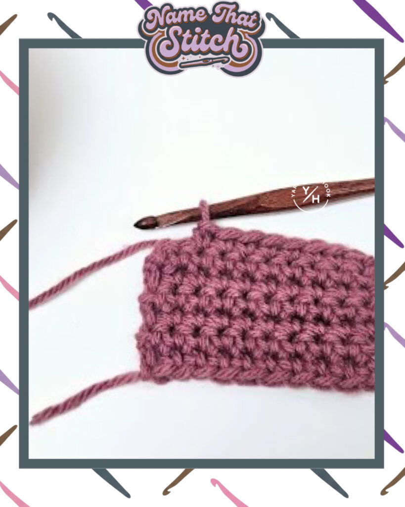 Close-up of a crocheted fabric displaying a repeating stitch pattern worked in purple yarn, with a wooden crochet hook and featured as part of the Name That Stitch daily crochet puzzle. View more at NameThatStitch.com