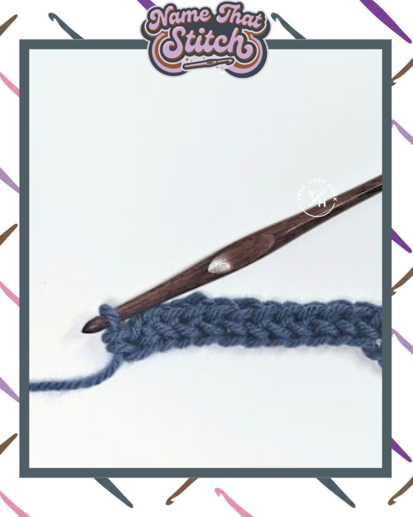 Close-up of a crocheted fabric displaying a repeating stitch pattern worked in blue yarn, with a wooden crochet hook and featured as part of the Name That Stitch daily crochet puzzle. View more at NameThatStitch.com
