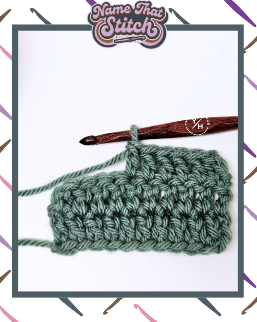 Close-up of a crocheted fabric displaying a repeating stitch pattern worked in green yarn, with a wooden crochet hook and featured as part of the Name That Stitch daily crochet puzzle. View more at NameThatStitch.com