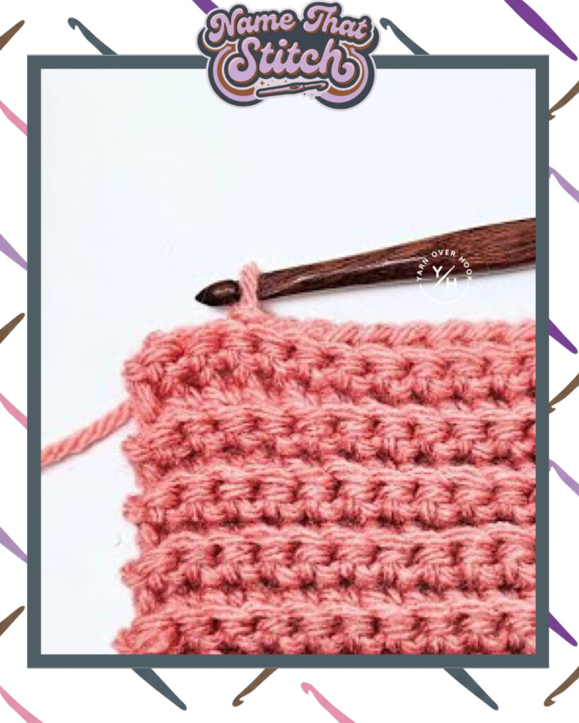 Close-up of a crocheted fabric displaying a repeating stitch pattern worked in Pink yarn, with a wooden crochet hook and featured as part of the Name That Stitch daily crochet puzzle. View more at NameThatStitch.com