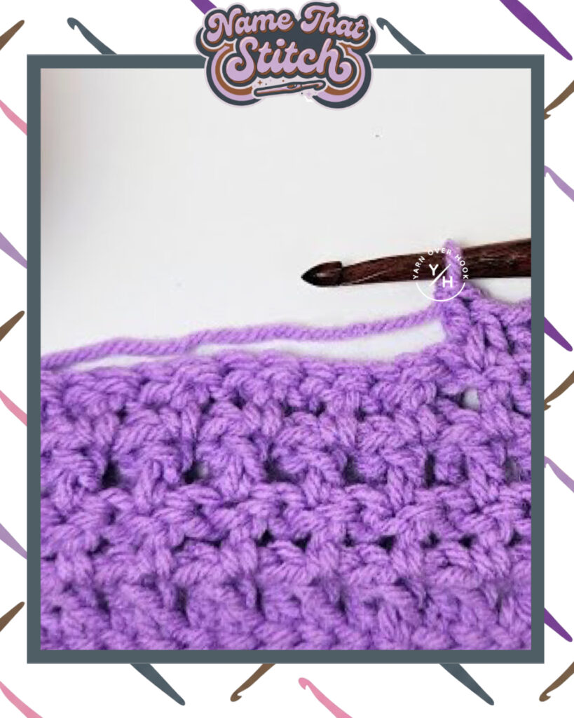 Close-up of a crocheted fabric displaying a repeating stitch pattern worked in purple yarn, with a wooden crochet hook and featured as part of the Name That Stitch daily crochet puzzle. View more at NameThatStitch.com