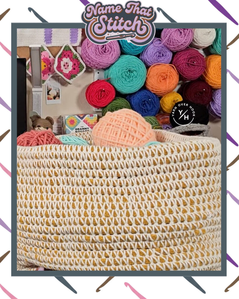 Large crocheted basket filled with pastel yarn balls, set in a colorful crochet studio with a wall display of bright yarn skeins and handmade crochet squares in the background. Featured as part of the Name That Stitch daily crochet puzzle. View more at NameThatStitch.com