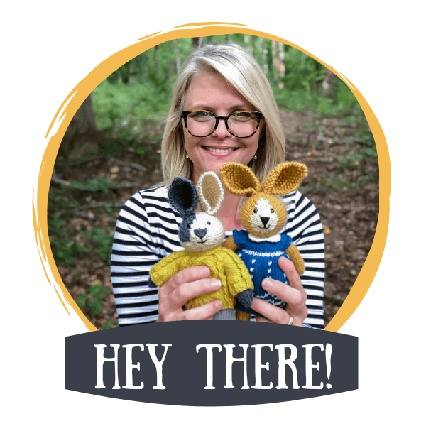 Woman (Elise Rose) with glasses smiling outdoors while holding two crocheted bunny dolls, framed by a yellow circle with the text “Hey There!” below.