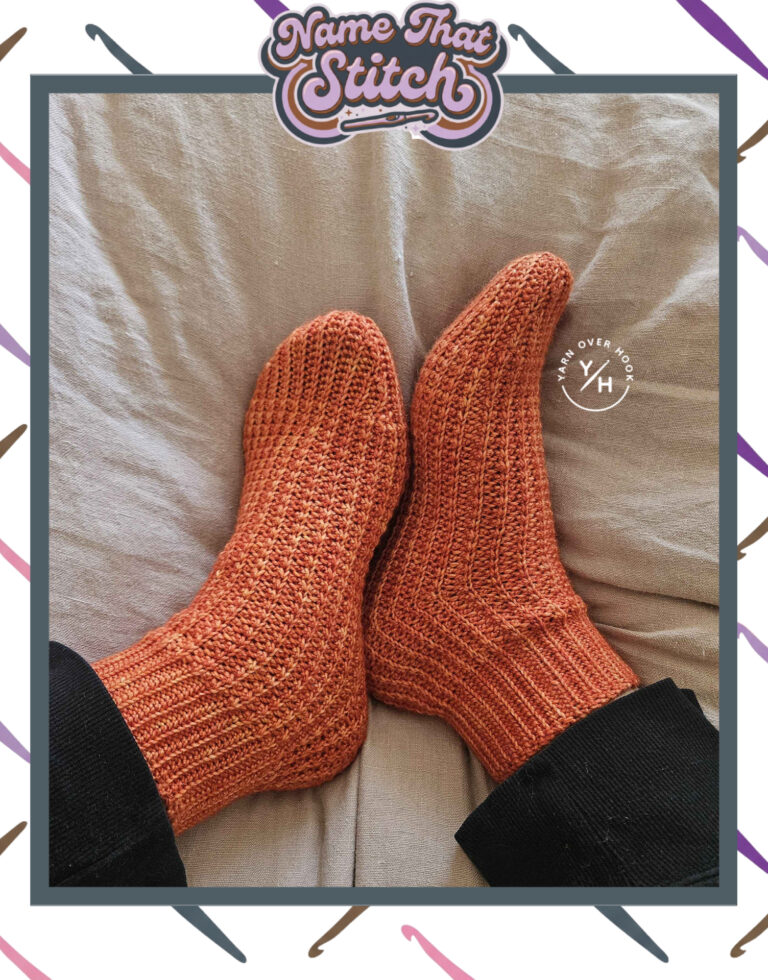 Close-up of a pair of crocheted socks worked in warm rust-colored yarn, displaying a textured stitch pattern and ribbed cuffs, featured as part of the Name That Stitch daily crochet puzzle. View more at NameThatStitch.com