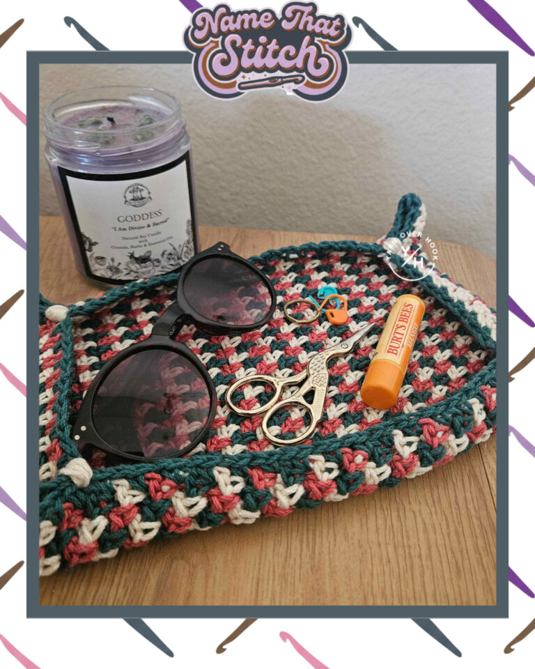 Close-up of a multicolored crocheted tray holding sunglasses, small scissors, stitch markers, lip balm, and a candle, displaying a repeating stitch pattern and featured as part of the Name That Stitch daily crochet puzzle. View more at NameThatStitch.com