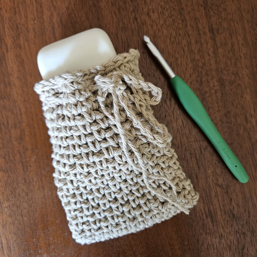 Handmade crocheted S.O.A.P. sack with a bar of soap beside a Clover ergonomic crochet hook, created for the Summer Stash Bash x S.O.A.P. S.A.C.K. community project.